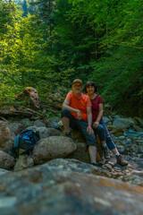 Ein Paar macht an einem heißen Sommertag ein Selfie in einem kühlen Bachbett. Ein Mann und eine Frau sitzen zwischen Felsen im Tal, Wanderer unterwegs im Schatten