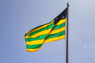 Uma bandeira do estado de Goiás hasteada e balançando ao vento com céu ao fundo.