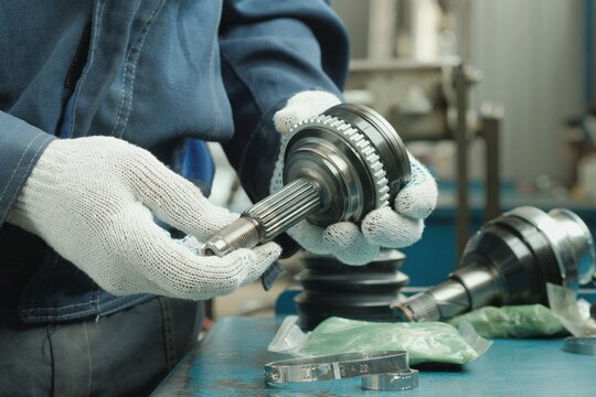 An auto mechanic inspects a joint of equal angular velocities. Checking and monitoring the compliance and integrity of the spare part of the car suspension.Maintenance and repair in the car center.