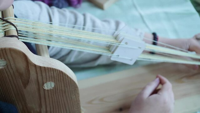 Close-up of a woman engaged in manual weaving of fabric separating the threads with bulkheads