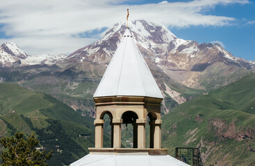 Kazbek 5054m mountain view with Gergeti village through the architectural arches of the chapel in Prophet Elijah Fathers Monastery on the green grass hill near Stepantsminda, East Caucasus, Georgia