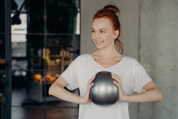 Sportive positive woman with red hair holding mini exercise ball