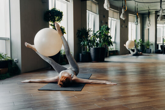 Fit Woman Training With Exercise Ball On Yoga Mat In Fitness Studio