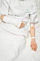 Vertical top-down shot of unrecognizable female patient with broken arm in cast receiving medication or nutrient fluids through IV line
