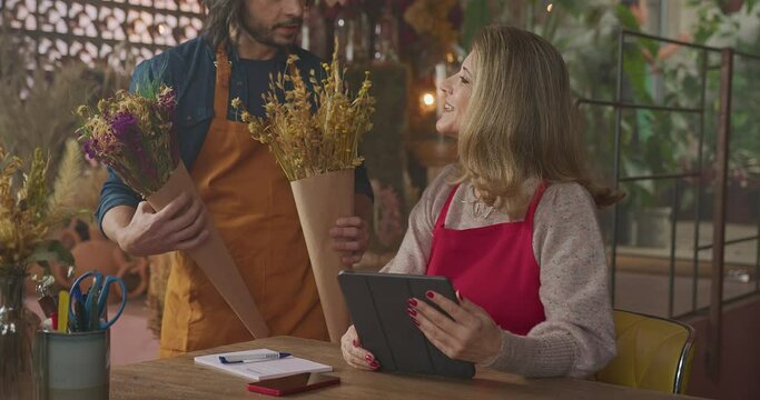 Male employee bringing two bouquet options for female entrepreneur to choose from for client. Small local business concept managing online orders for customers