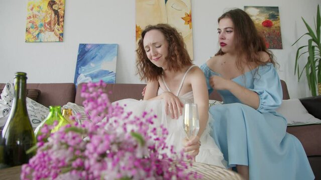 4K. A sad bride in a white wedding dress is crying on the couch, her friend calms her down