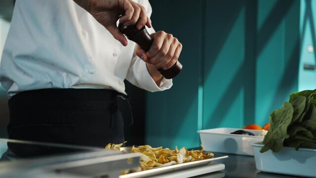 Close up: the chef is using pepper mill to add some pepper to his food, salt is falling in slow motion, grinding pepper using kitchen stuff