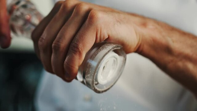 Macro shot: the chef is using a salt mill to add some salt to his food, salt is falling in slow motion, grinding salt using kitchen stuff