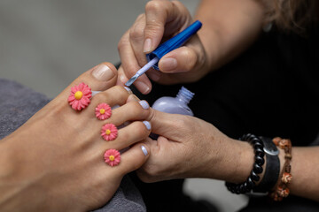 Specialist in a beauty salon giving a pedicure by painting toenails with glossy paint.