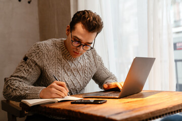 Young white man wearing eyeglasses working on laptop in cafe