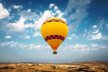 Hot air balloon flying over rock and valley landscape at Cappadocia - Goreme, Turkey. Yellow baloon...