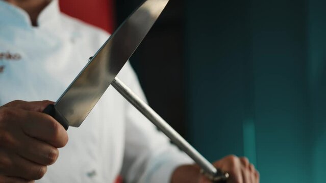 Restaurant kitchen: male chef sharpening knives before cooking steak