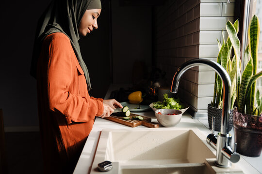 Side view of calm young woman in hijab cutting vegetables