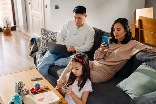 Young Asian Family Sitting On Couch In Cozy Living Room