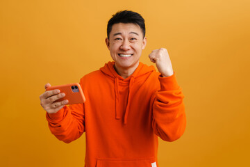 Happy brunette asian adult man rejoicing while holding cellphone