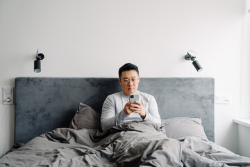 Asian man using mobile phone after sleep while sitting in bed