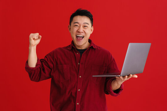Asian excited man making winner gesture while using laptop