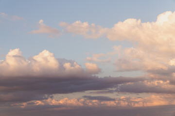 Beautiful well balanced sky replacement sunset background with layers of fluffy white cumulus clouds with pink and yellow hues on a blue sky background.