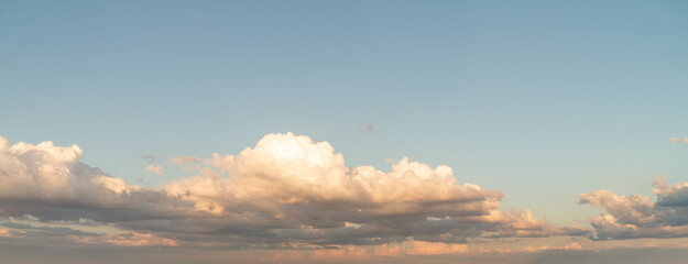 Obraz premium Beautiful panoramic sky replacement sunset background starting at the horizon with layers of fluffy white yellow and pink hued cumulus clouds on a blue sky background.