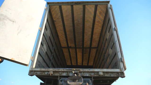 Driver closes doors on trailer of parked truck at summer sunny day. Lorry parked in the countryside. Bottom view Slow motion Close up
