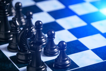 Black chess pieces on chess board with bright blue background light.