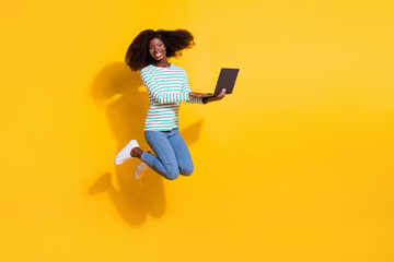 Full size photo of active energetic lady hold use wireless netbook jumping isolated on yellow color background