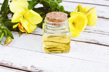 Obraz na płótnie Canvas Essential oil of evening primrose in glass bottle, yellow flowers on white table, alternative medicine