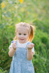Happy little girl 3 years old in a sunflower field in the sun. Cute child holding a flower in his hands. Summer.