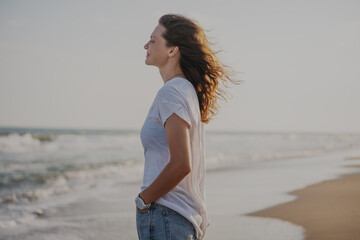 Young beautiful smiling cheerful woman in white t-shirt standing on the seashore enjoying vacation