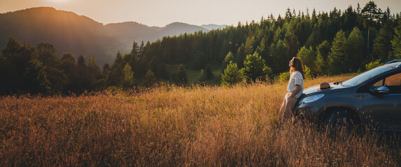 Young beautiful woman traveler enjoying the sunset in the mountains while traveling by car