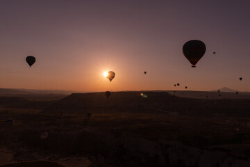 Sunrise in Cappadocia, with the sun eclipsed by a hot air balloon, with an orange and pink sky.
