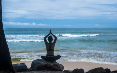 Back view woman doing yoga on the rock at sea, Yoga concept
