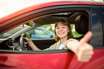 Happy teen girl driving a new car on sunset