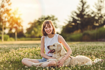 Portrait of teenage girl petting golden retriever outside in sunset