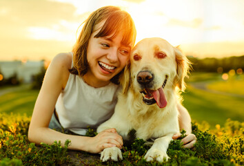 Portrait of teenage girl petting golden retriever outside in sunset showing tongue