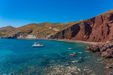 Fototapeta na wymiar Beautiful scenery of red sand beach with a boat in Akrotiri village on Santorini, Greece