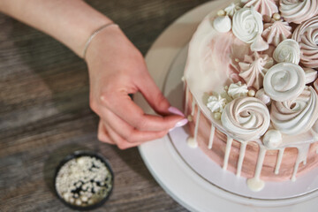 beautiful female hands lay out pearl beads and meringues and marshmallows of different shapes, decorating a beautiful festive pink birthday cake