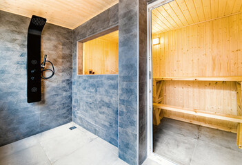 Real estate photography of a brand new wooden sauna interior and a modern shower area with dark...