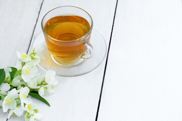 Jasmine tea in glass cup and flowers on a wooden white background. Cup with green jasmin tea. Tea time