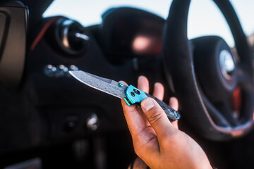 Showing a open Damascus blade pocket knife in front of a steering wheel - obrazy, fototapety, plakaty