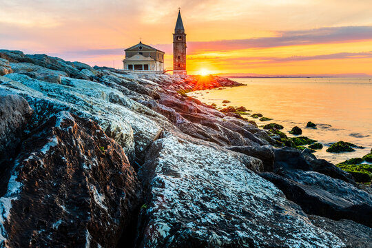 The city of Caorle in Italy at sunrise and its landmark on the main promenade, the Santuario della Madonna dell'Angelo church located right by the sea