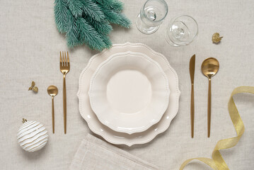 Christmas table setting on a beige linen tablecloth. Top view, flat lay. Beige plates, golden...