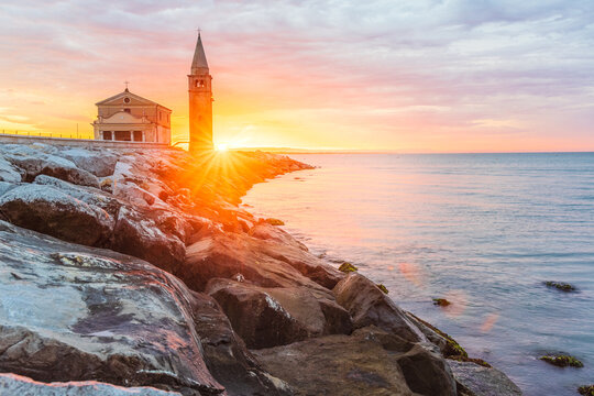 The city of Caorle in Italy at sunrise and its landmark on the main promenade, the Santuario della Madonna dell'Angelo church located right by the sea