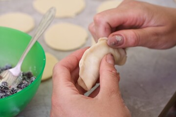 A woman is making dumplings with blueberries. Puts the berries in the rolled out dough and fixes. Close-up.