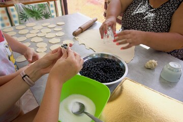 A woman prepares dough for dumplings with blueberries. Another woman puts stuffing in the dough.
