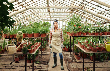 Horizontal long shot of young adult Hispanic woman wearing apron and rubber boots standing in...