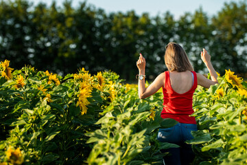 Kobieta relaksująca się w otoczeniu natury. Dziewczyna w czerwonej bluzce stojąca w polu słoneczników. Kontakt z naturą w leczeniu stresu i psychiki. - obrazy, fototapety, plakaty