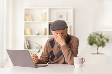 Elderly man having a headache and holding a document and sitting in front of a laptop computer
