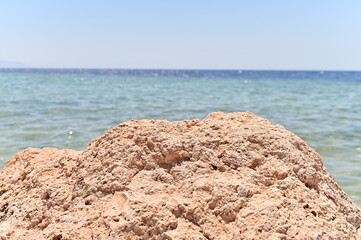 Background for cosmetics on the beach with sand. The podium is made of natural stone. A mock-up of a pedestal in the sunlight with a view of the sea.
