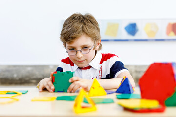 Happy kid boy with glasses having fun with building and creating geometric figures, learning mathematics and geometry